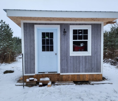 Front view of a snowy 10' x 12' Urban Studio with grey siding and white doors & windows